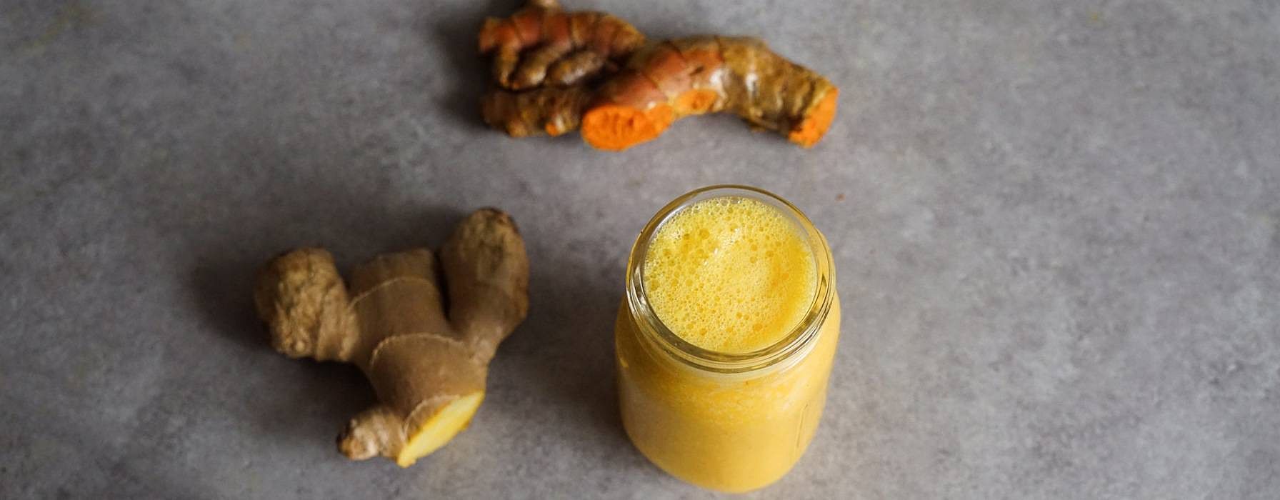 Ingwerknolle und Kurkumaknolle neben einem Glas mit Ingwer Shot