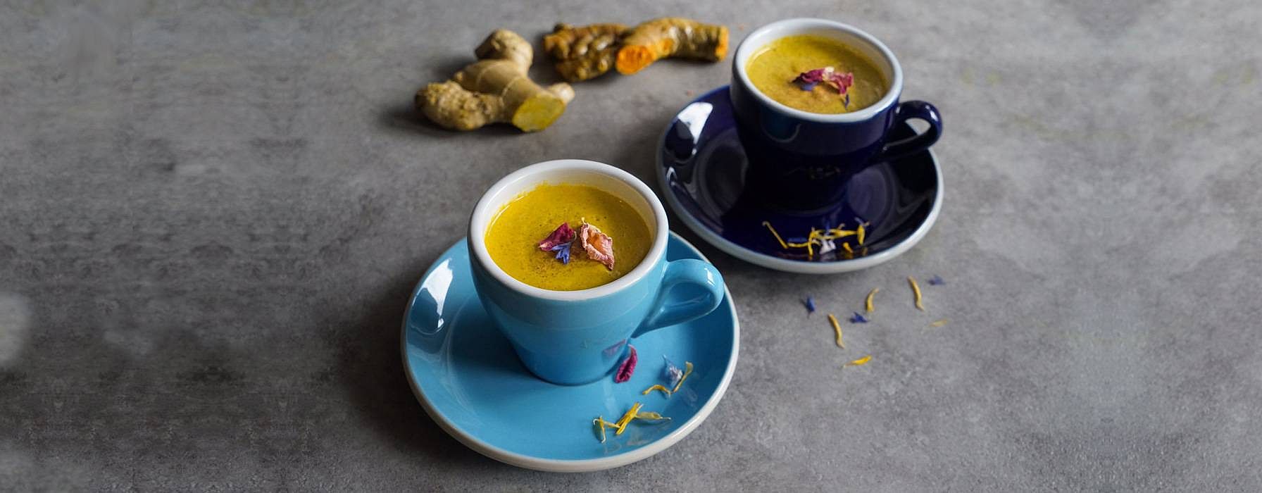 zwei blaue Tassen mit veganer Moonmilk, in Hintergrund liegt eine gelbe Kurkumawurzel