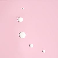 Les gouttes blanches du soin lissant pour les yeux Weleda sur un fond rose