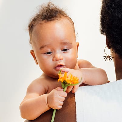 baby spielt mit calendulablüte auf dem arm der mutter