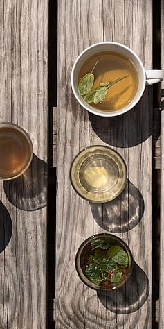 Cups with tea and glasses of water on wooden floorboards.