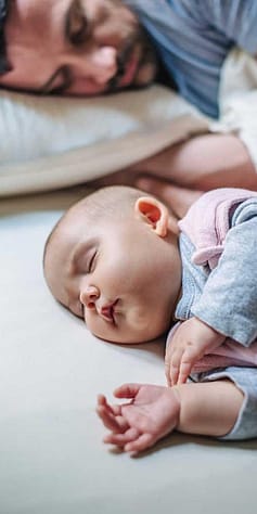 Baby sleep on his sad and dad behind.