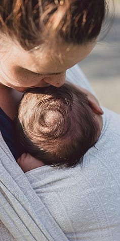Mother carrying baby in a sling and kissing his head