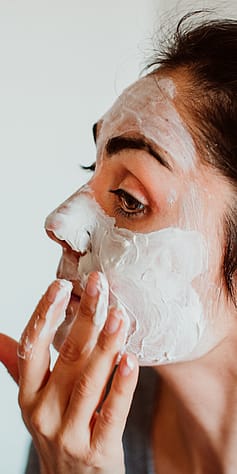 Žena v koupelně aplikuje čistící pleťovou masku