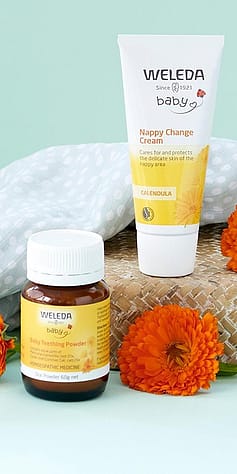Baby Teething Powder and Calendula Nappy Change Cream next to orange flowers.