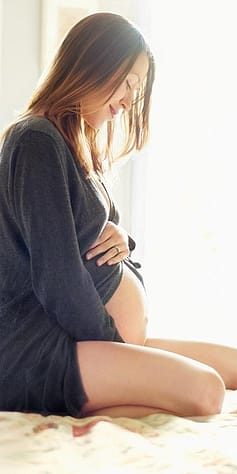 Donna incinta seduta in ginocchio sul letto che si accarezza il ventre