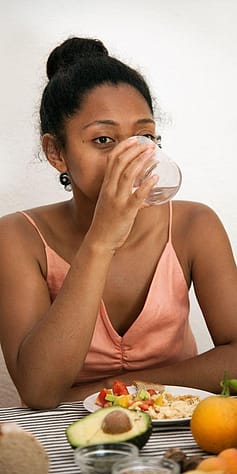 Frau trinkt Wasser und hat gesundes Essen vor sich