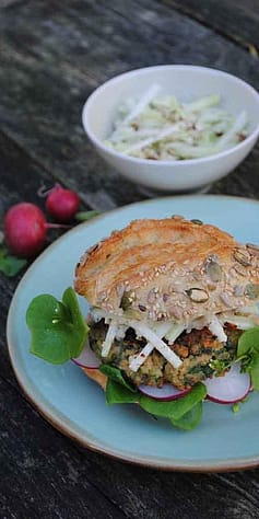 Der fertige Burger mit Salatblatt und Radieschen liegt angerichtet auf einem Teller