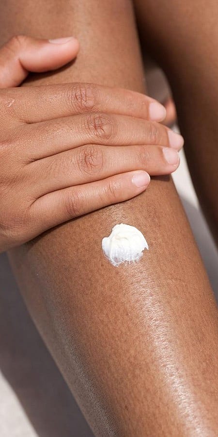 Jeune femme applique crème sur sa jambe
