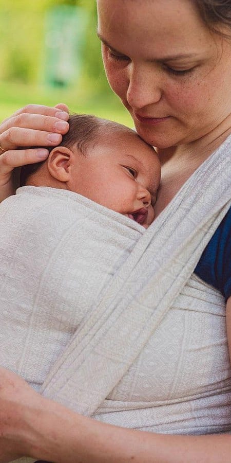 Mamma tiene il neonato in una fascia e poggia la mano sulla sua testolina