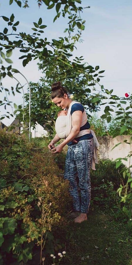 Mamma tiene il bambino in fascia mentre lavora il terreno con le mani