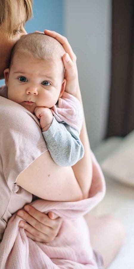 Mamma tiene in braccio neonato appoggiando una mano sulla sua testa