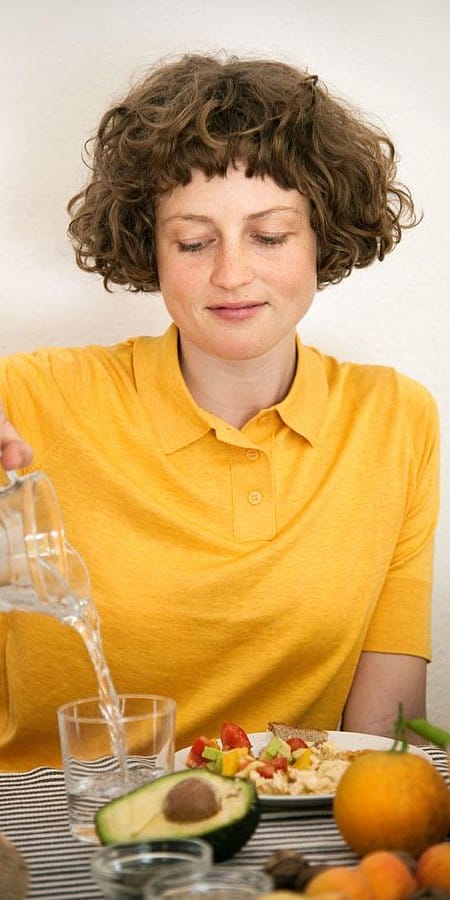 Frau schenkt sich beim Essen Wasser in ein Glas