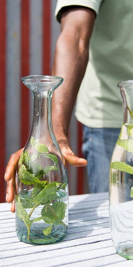 Mano afferra una bottiglia di vetro che ha all'interno acqua e menta