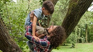 Man holding a child above his arms in a forest.