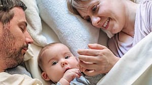 bebe tumbado en la cama con sus padres