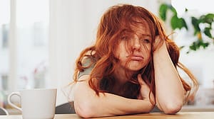 Frau sitzt muede neben einer Tasse Kaffee