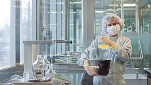 Lab assistant holding a large transparent container filled with a dark liquid