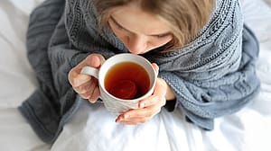 Frau ist eingehuellt in einen dicken Schal und trinkt Tee