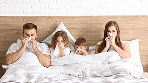 Familie im Bett alle schneuzen sich