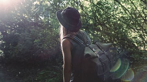 Frau mit Rucksack wandert am Waldrand entlang