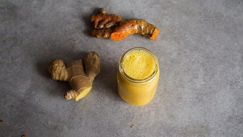 Ingwerknolle und Kurkumaknolle neben einem Glas mit Ingwer Shot