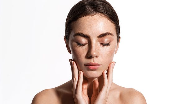 Entspannte junge Frau haelt ihr Gesicht in den Haenden