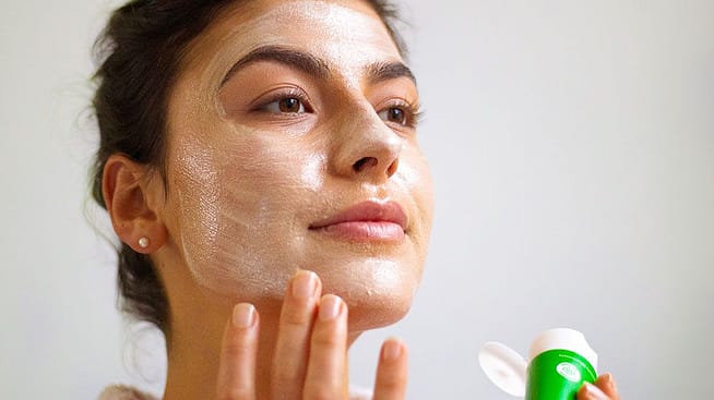 junge frau trägt weleda skin food im gesicht auf