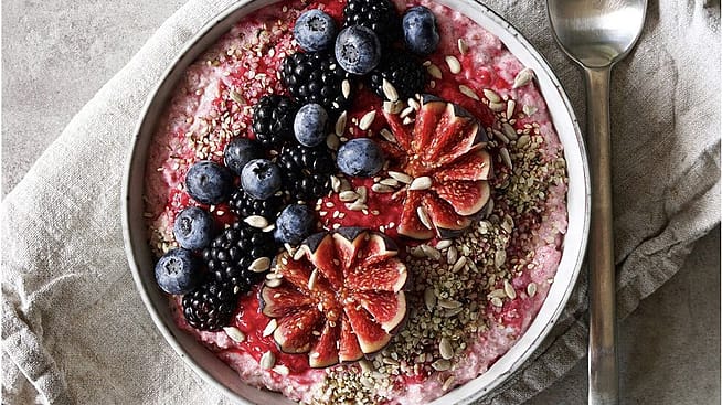 Blick von oben auf eine Bowl mit Muesli garniert mit frischen Brombeeren, Heidelbeeren, Feigen und Saaten