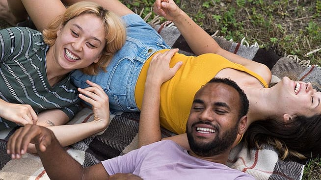 Zwei Frauen und ein Mann liegen auf einer Decke in der Natur