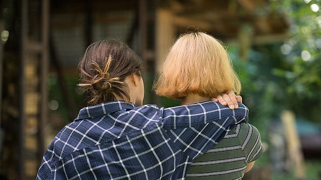 Zwei Frauen von hinten, eine legt den Arm um die Schulter der anderen