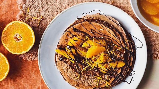 Mehrere Schokoladen-Crèpes auf einem Teller garniert mit marinierten Orangen und Schokoladensauce