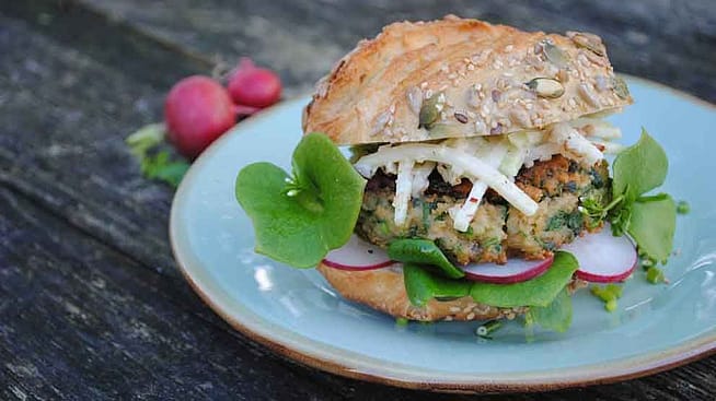 Der fertige Burger mit Radieschen und Salatblaettern liegt angerichtet auf einem Teller