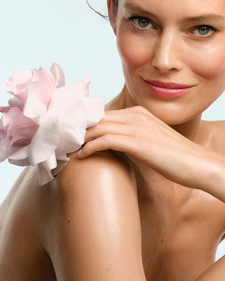 Sitzende Frau, die einen Arm über ihre Schulter legt. In der Hand hält sie eine Wildrosenblüte.