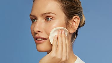 model applying Refining Toner to cheek with cotton round
