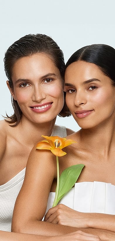 Zwei Frauen mit Lächeln stehen hintereinander, eine davon hält eine Blume in der Hand