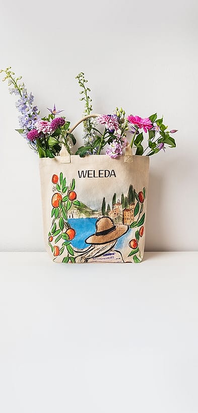 Strandtasche mit maritimem Design und Weleda-Schriftzug, gefüllt mit Blumen