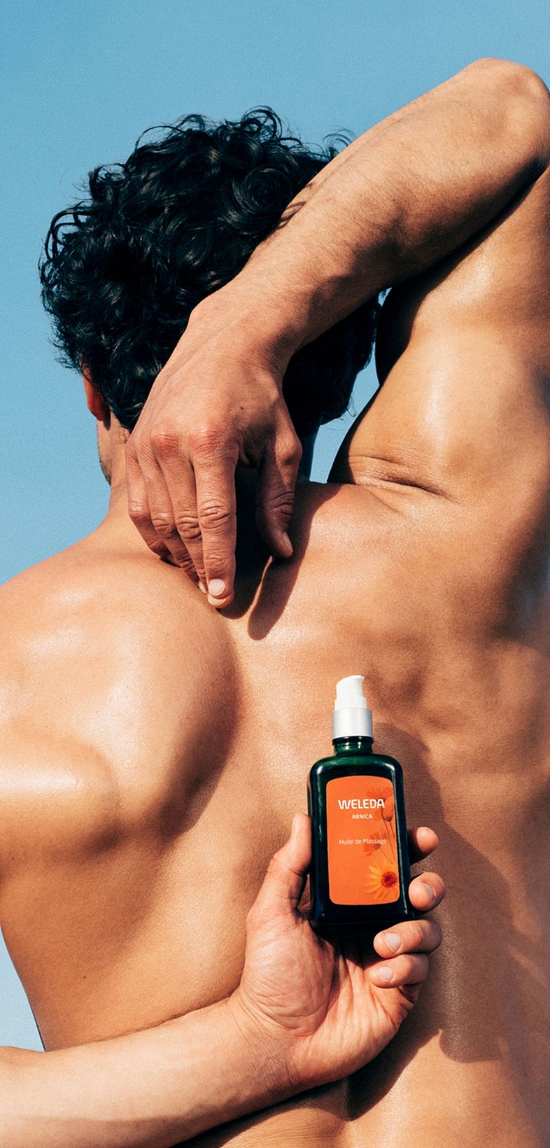 Des mains d'hommes tiennent un produit Weleda à l'arnica sur le dos.