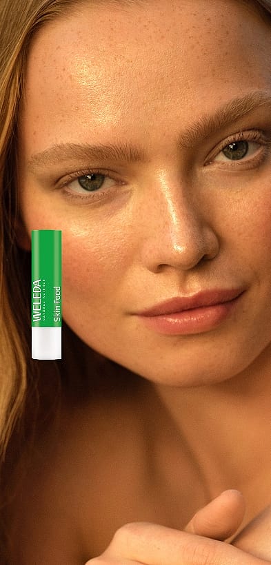 Frontale Ansicht einer Frau mit neutralem Gesichtsausdruck. Außerdem Abbildung des neuen Weleda Skin Food Lip Balm