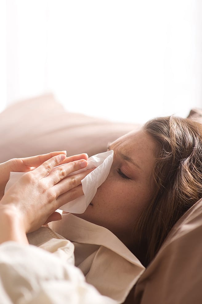 Frau im Bett schneuzt sich die Nase