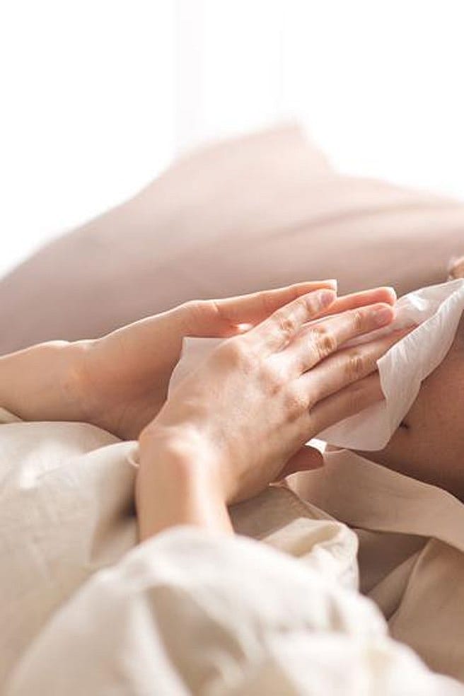 Frau im Bett schneuzt sich die Nase