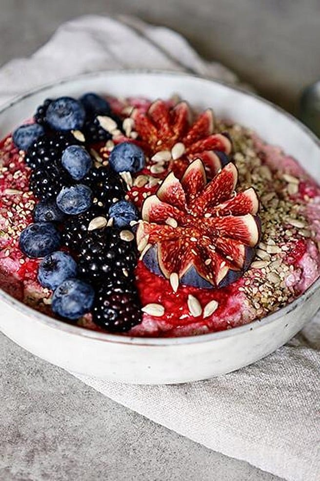 Bowl mit Muesli garniert mit frischen Brombeeren, Heidelbeeren, Feigen und Saaten
