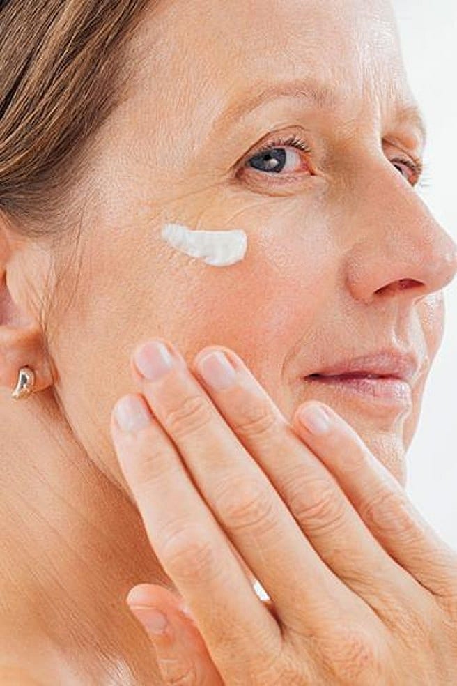 Frau traegt Creme auf Wange auf