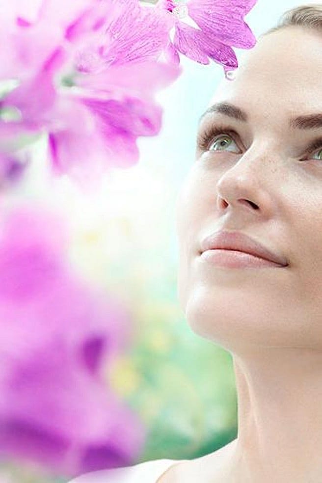 Frau mit Malvenblüten im Hintergrund schaut in den Himmel