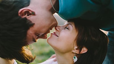 Ein Mann beugt sich von oben ueber eine Frau und gibt ihr einen Kuss