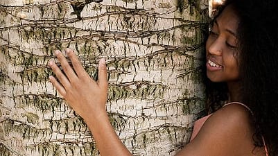 dark skinned woman hugging a tree.