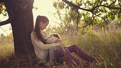 Une femme allaite, assise sous un arbre