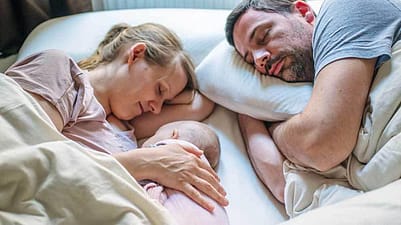 mujer, hombre y bebé tumbados en una cama mientras duermen