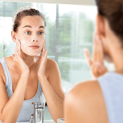 mujer limpiándose la cara mientras se mira al espejo