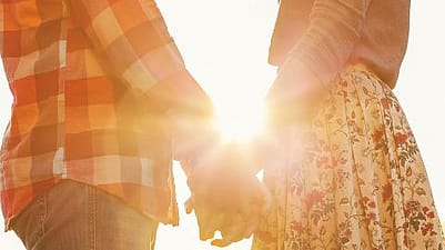 pareja agarrada de la mano en una puesta de sol